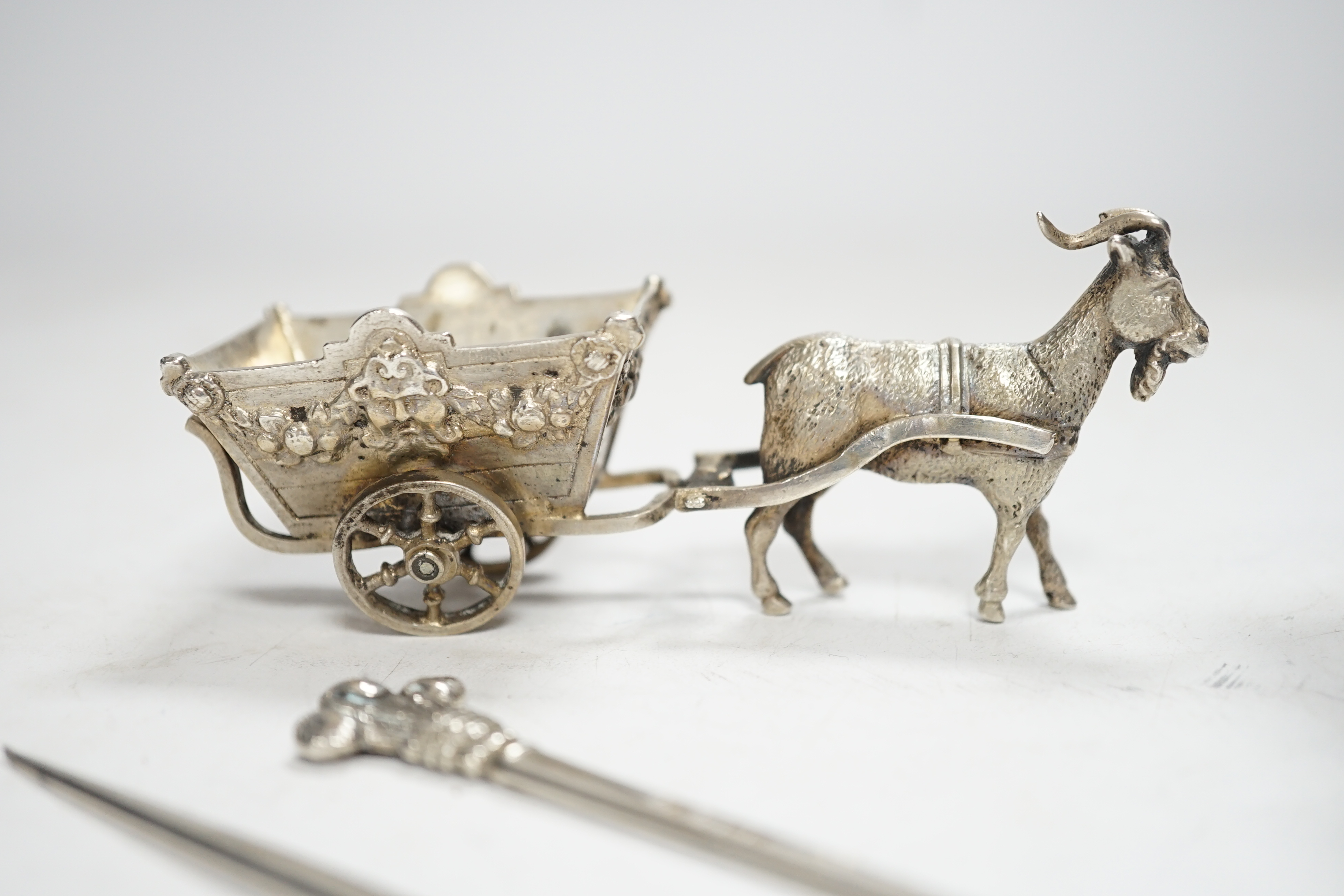 A pair of George V silver game skewers, with Prince of Wales feathers terminals, Atkin Brothers, Sheffield, 1915, 10.1cm, a Hanau? white metal miniature model of a goat pulling a cart and a Dutch white metal miniature mo